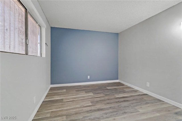 empty room with baseboards, a textured ceiling, and wood finished floors