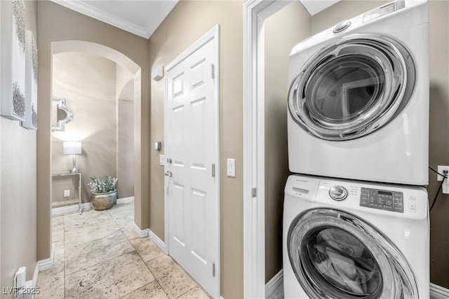 laundry area featuring crown molding, baseboards, laundry area, stacked washer and clothes dryer, and arched walkways