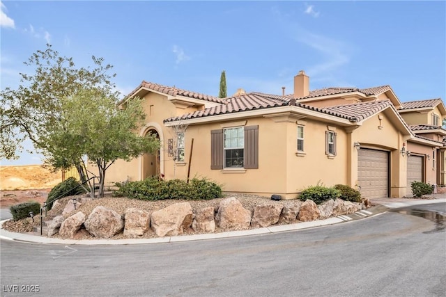 mediterranean / spanish-style house featuring stucco siding, driveway, a tile roof, an attached garage, and a chimney