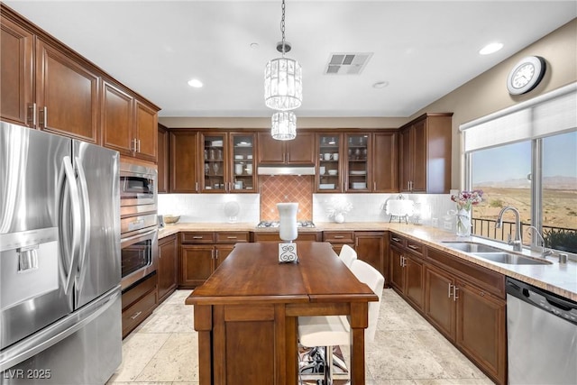 kitchen with appliances with stainless steel finishes, tasteful backsplash, a kitchen island, pendant lighting, and sink