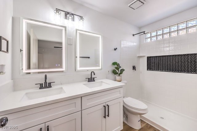 bathroom with hardwood / wood-style flooring, vanity, toilet, and a tile shower