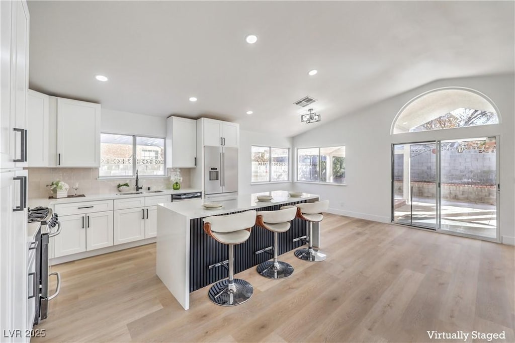 kitchen featuring lofted ceiling, sink, white cabinetry, stainless steel appliances, and a kitchen island