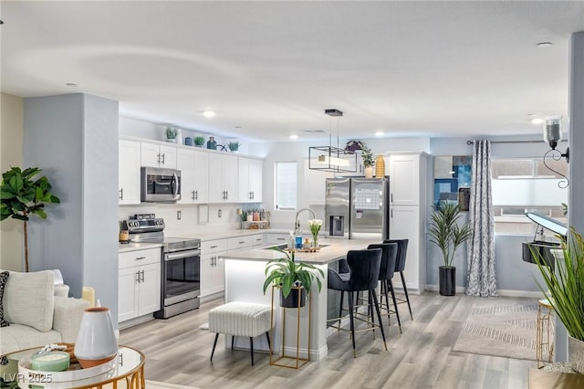 kitchen featuring white cabinets, a center island with sink, sink, light hardwood / wood-style flooring, and appliances with stainless steel finishes