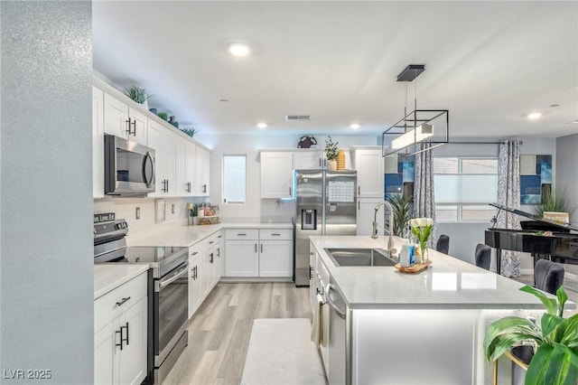 kitchen with stainless steel appliances, white cabinetry, a kitchen island with sink, and light hardwood / wood-style flooring