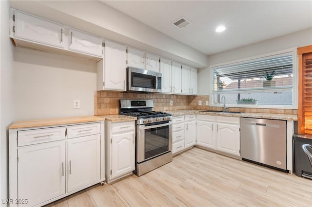 kitchen featuring light wood-type flooring, backsplash, stainless steel appliances, sink, and white cabinetry