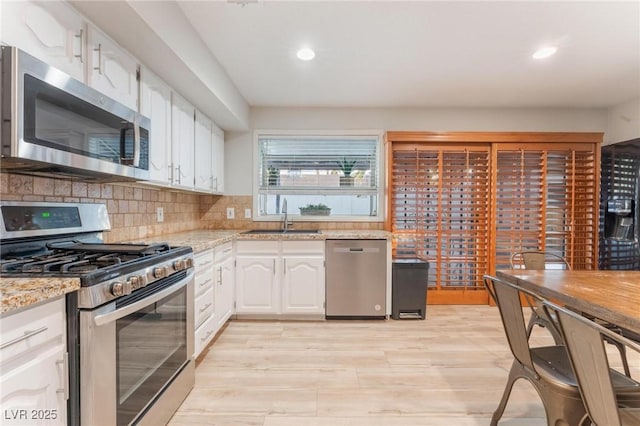 kitchen with light stone countertops, white cabinetry, sink, stainless steel appliances, and decorative backsplash