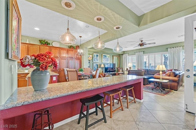 kitchen with ceiling fan, light tile patterned floors, decorative light fixtures, a kitchen island, and a breakfast bar area