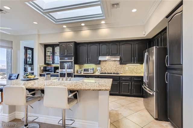 kitchen featuring light tile patterned flooring, appliances with stainless steel finishes, a center island with sink, and a kitchen bar