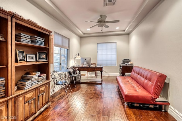 office space with dark wood-type flooring, a raised ceiling, and ceiling fan