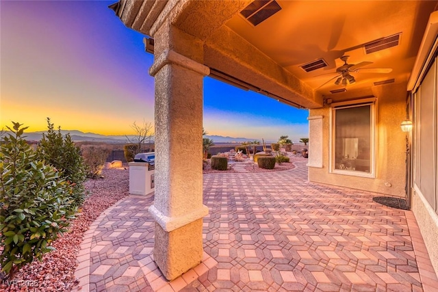 patio terrace at dusk featuring a mountain view, ceiling fan, and a grill