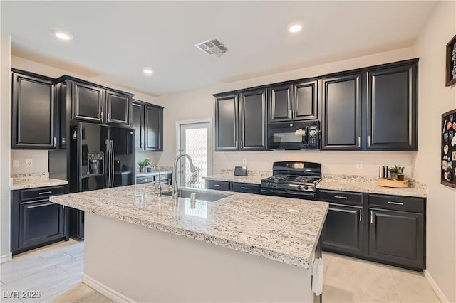 kitchen featuring light stone countertops, a kitchen island with sink, sink, black appliances, and light tile patterned flooring