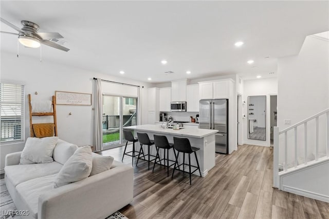 kitchen featuring ceiling fan, a kitchen bar, a center island with sink, white cabinets, and appliances with stainless steel finishes