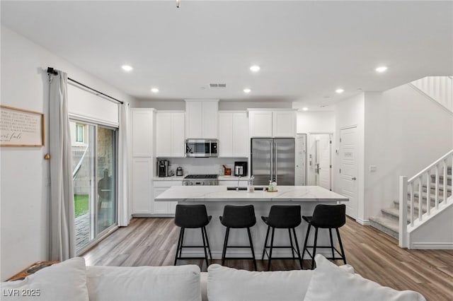 kitchen featuring appliances with stainless steel finishes, white cabinetry, a kitchen breakfast bar, and an island with sink