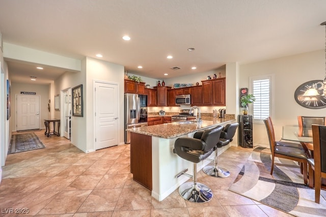 kitchen with a kitchen bar, light stone counters, light tile patterned floors, appliances with stainless steel finishes, and kitchen peninsula