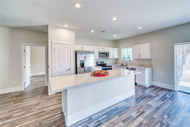 kitchen featuring white cabinetry, a center island, sink, stainless steel appliances, and light stone counters