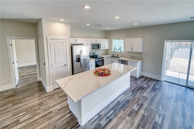 kitchen featuring appliances with stainless steel finishes, light stone counters, sink, a center island, and white cabinetry