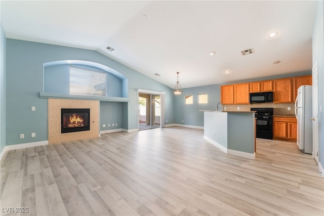 kitchen with lofted ceiling, black appliances, a center island with sink, a fireplace, and tasteful backsplash