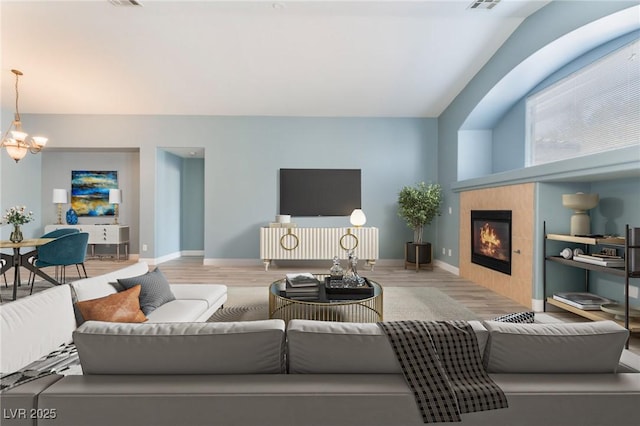 living room featuring a notable chandelier, a tile fireplace, and light hardwood / wood-style flooring