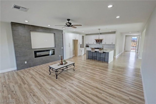 living room featuring ceiling fan, a large fireplace, and light hardwood / wood-style floors