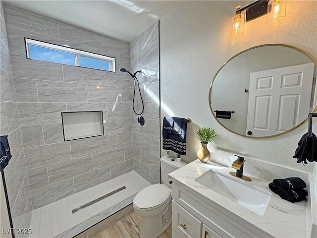 bathroom with a tile shower, vanity, and toilet