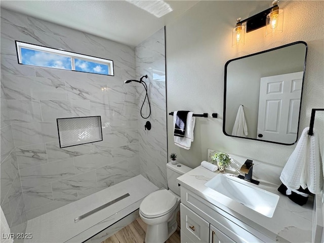 bathroom featuring hardwood / wood-style flooring, vanity, toilet, and a tile shower