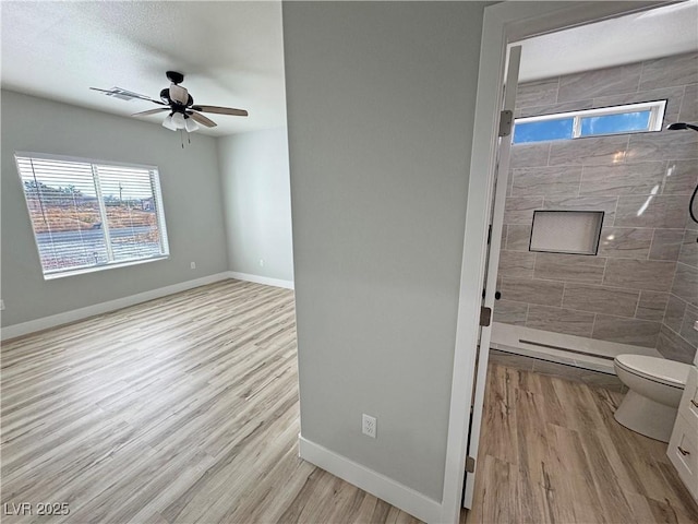 bathroom with hardwood / wood-style floors, toilet, ceiling fan, and a tile shower