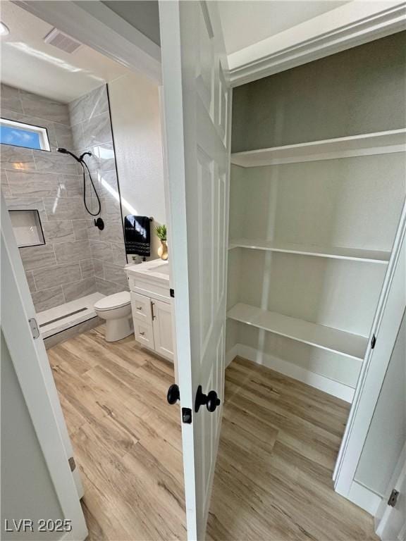 bathroom featuring toilet, wood-type flooring, vanity, and a tile shower