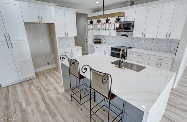 kitchen with white cabinetry, sink, stainless steel appliances, pendant lighting, and a center island with sink