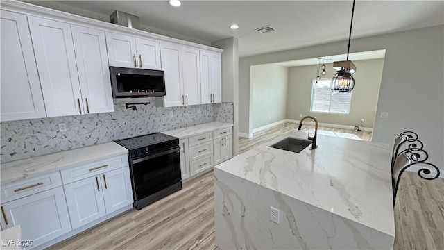 kitchen featuring black range with electric stovetop, sink, light stone counters, decorative light fixtures, and white cabinets