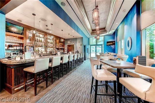 bar featuring decorative light fixtures, a raised ceiling, ornamental molding, and light stone counters