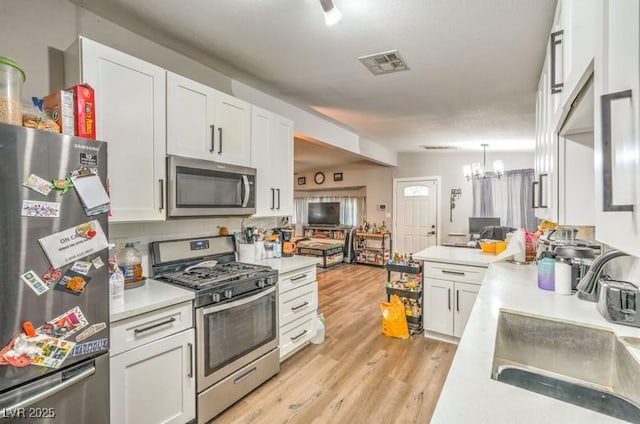 kitchen with an inviting chandelier, white cabinets, sink, decorative backsplash, and stainless steel appliances