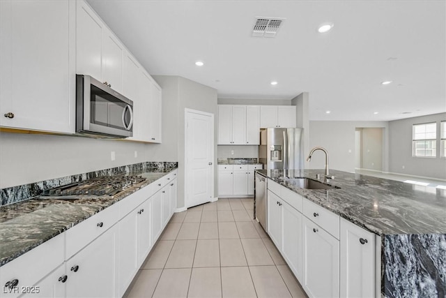 kitchen with sink, light tile patterned floors, dark stone countertops, white cabinets, and appliances with stainless steel finishes