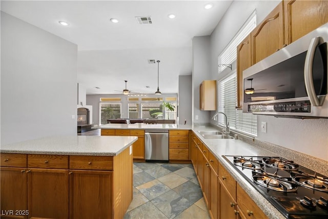 kitchen with a wood stove, hanging light fixtures, sink, appliances with stainless steel finishes, and kitchen peninsula