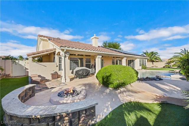 rear view of property featuring solar panels, a patio area, an outdoor fire pit, and a swimming pool