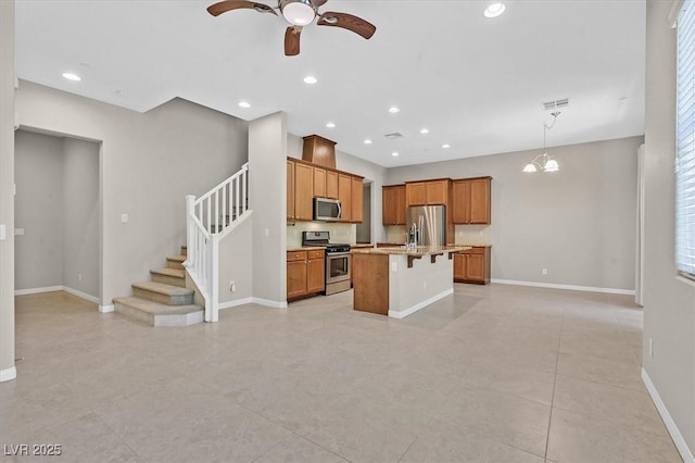 kitchen featuring a kitchen bar, ceiling fan with notable chandelier, stainless steel appliances, pendant lighting, and a center island with sink