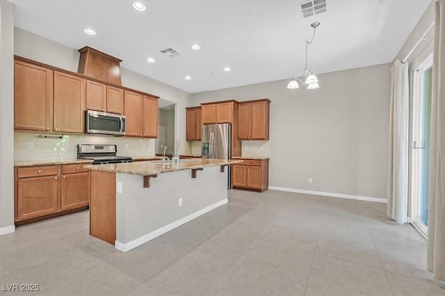 kitchen featuring a kitchen breakfast bar, light stone counters, a notable chandelier, a center island with sink, and appliances with stainless steel finishes