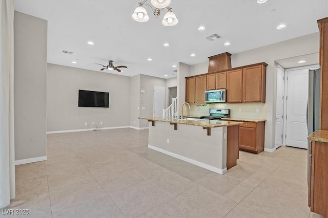 kitchen with a breakfast bar, ceiling fan with notable chandelier, sink, appliances with stainless steel finishes, and light stone counters