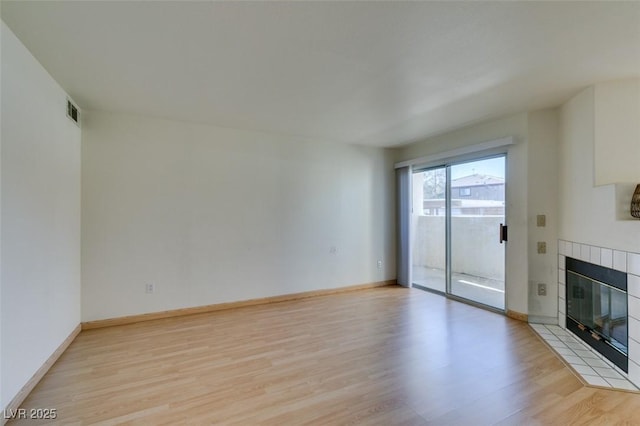 unfurnished living room with a tile fireplace, baseboards, visible vents, and light wood finished floors