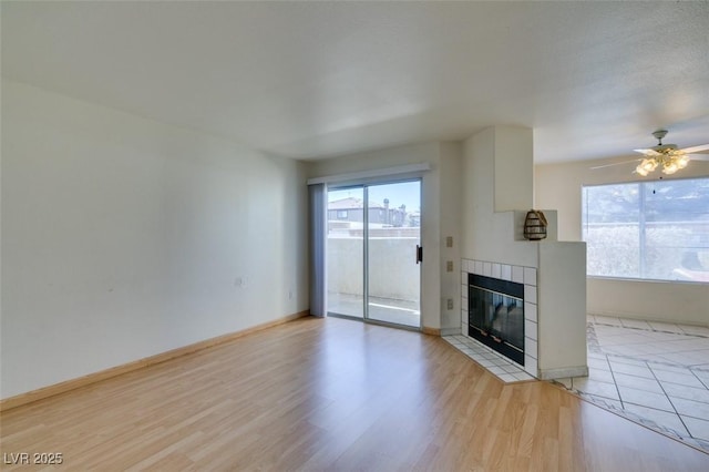 unfurnished living room featuring ceiling fan, light wood-type flooring, a tiled fireplace, and baseboards