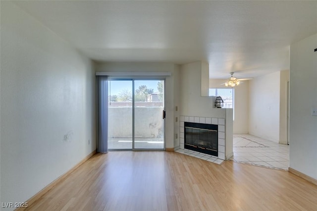 unfurnished living room with ceiling fan, a tile fireplace, light wood-style flooring, and baseboards