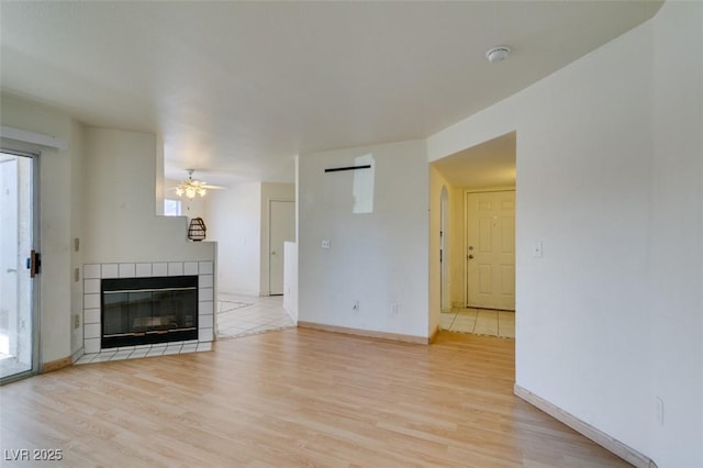 unfurnished living room featuring a tile fireplace, light hardwood / wood-style flooring, and ceiling fan