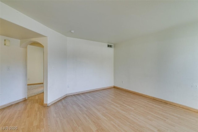 empty room featuring arched walkways, visible vents, light wood-style flooring, and baseboards