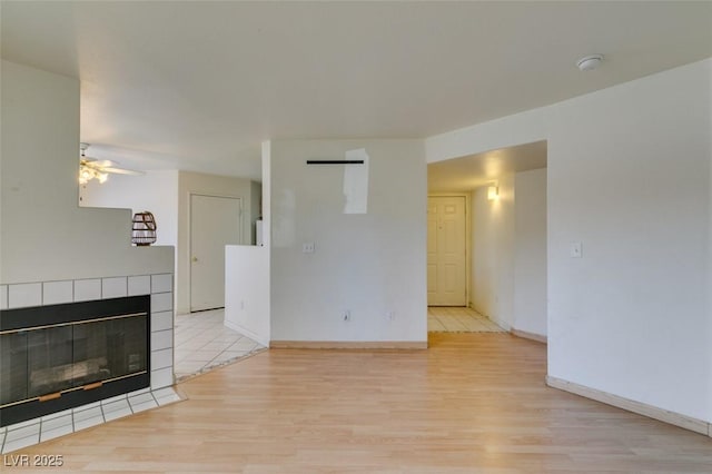 unfurnished living room featuring ceiling fan, a fireplace, baseboards, and wood finished floors