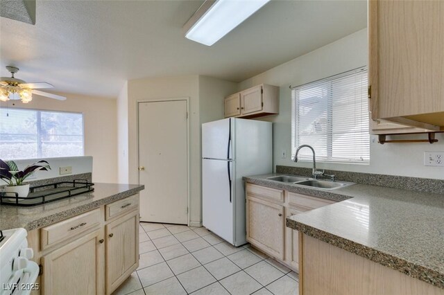 kitchen with light brown cabinetry, stove, ceiling fan, sink, and white fridge