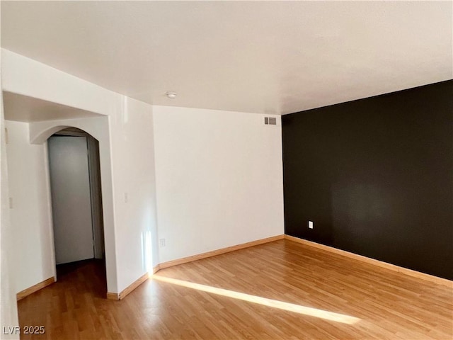 unfurnished room featuring arched walkways, visible vents, baseboards, and wood finished floors