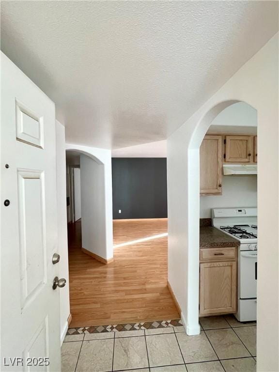 kitchen featuring light tile patterned floors, dark countertops, a textured ceiling, under cabinet range hood, and white gas range oven