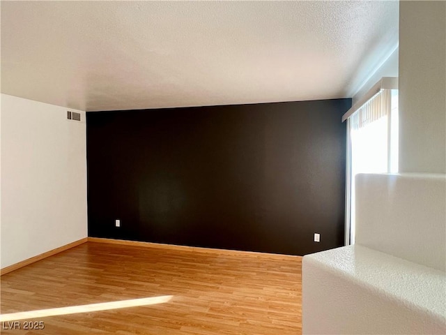 empty room featuring light wood-type flooring, baseboards, visible vents, and a textured ceiling