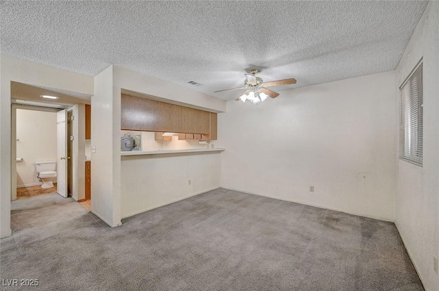 interior space featuring ceiling fan, light colored carpet, kitchen peninsula, and a textured ceiling