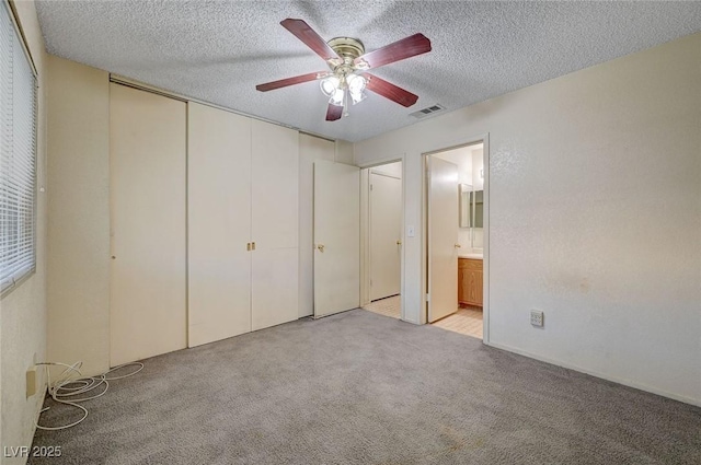 unfurnished bedroom featuring light carpet, a textured ceiling, ensuite bathroom, and ceiling fan