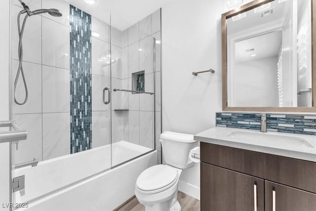 full bathroom featuring shower / bath combination with glass door, hardwood / wood-style floors, tasteful backsplash, toilet, and vanity